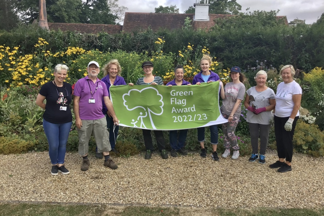 Group of Harlow Museum staff holding green flag in front of flower garden