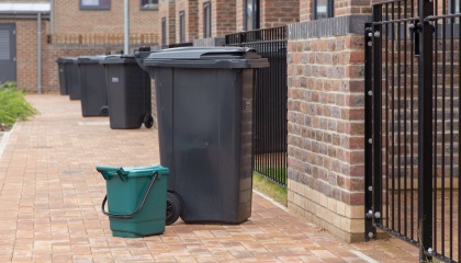 Image of green food waste bin next to black wheelie bin on side of street