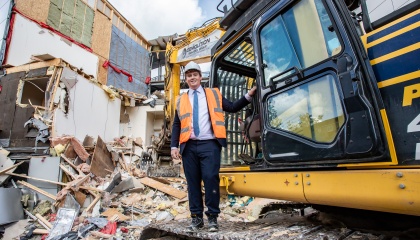 Councillor Dan Swords standing with a mechanical digger on the Occasio House demolition site
