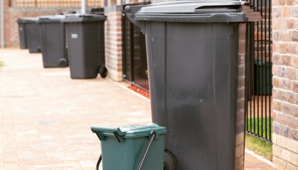 Image of back non-recycling bin and green food waste bin on the street outside houses