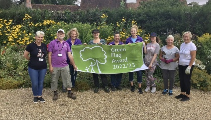 Group of Harlow Museum staff holding green flag in front of flower garden